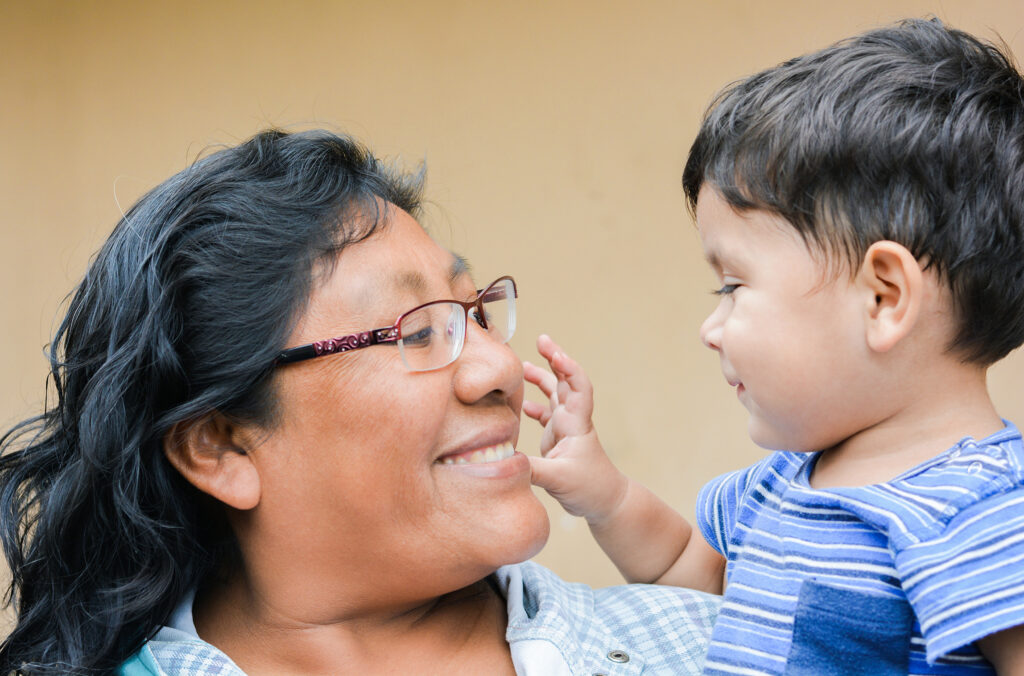 Mom smiles and looks at her toddler son as he reaches out to her face